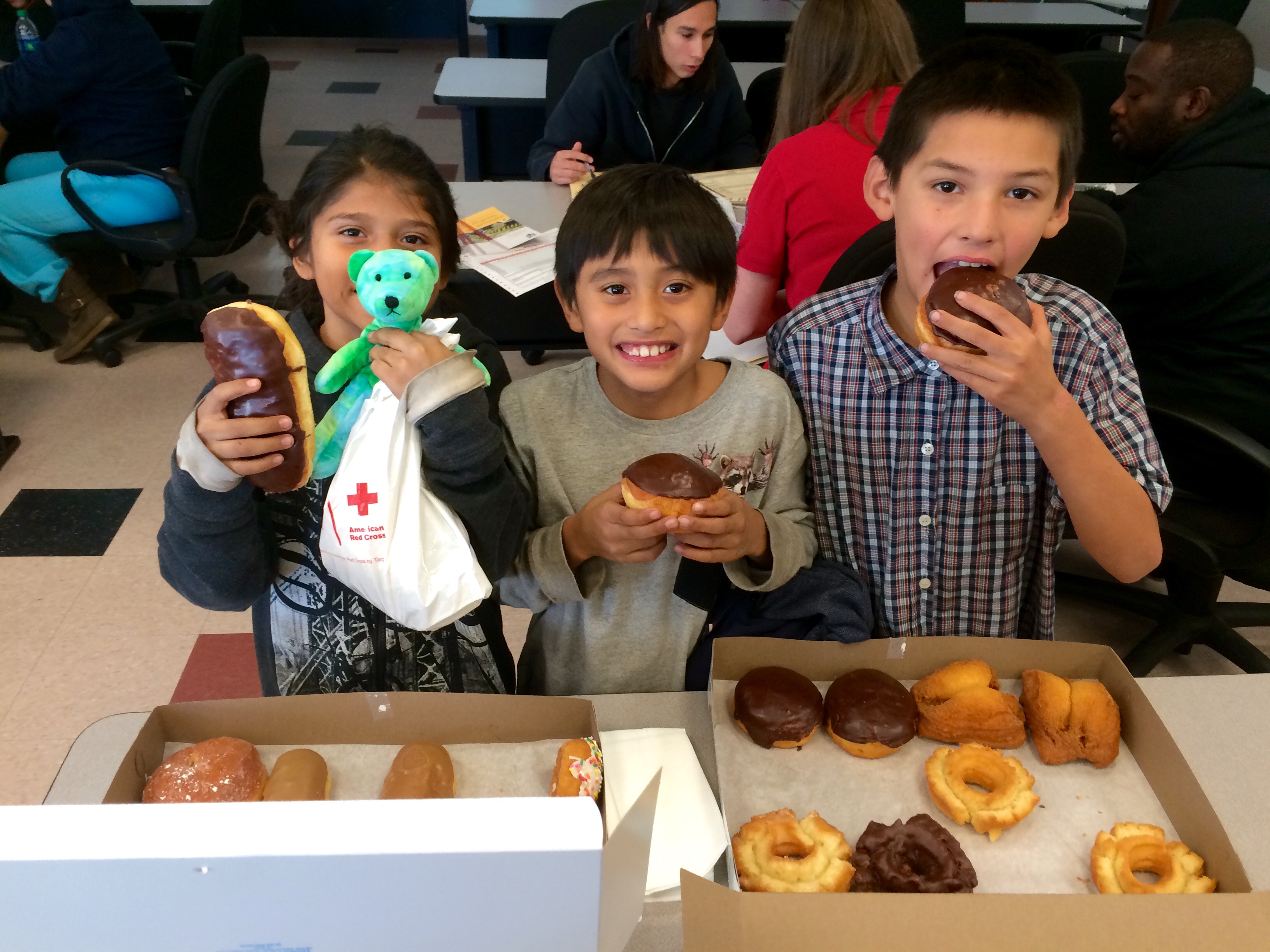 Three smiling children while eating donuts.