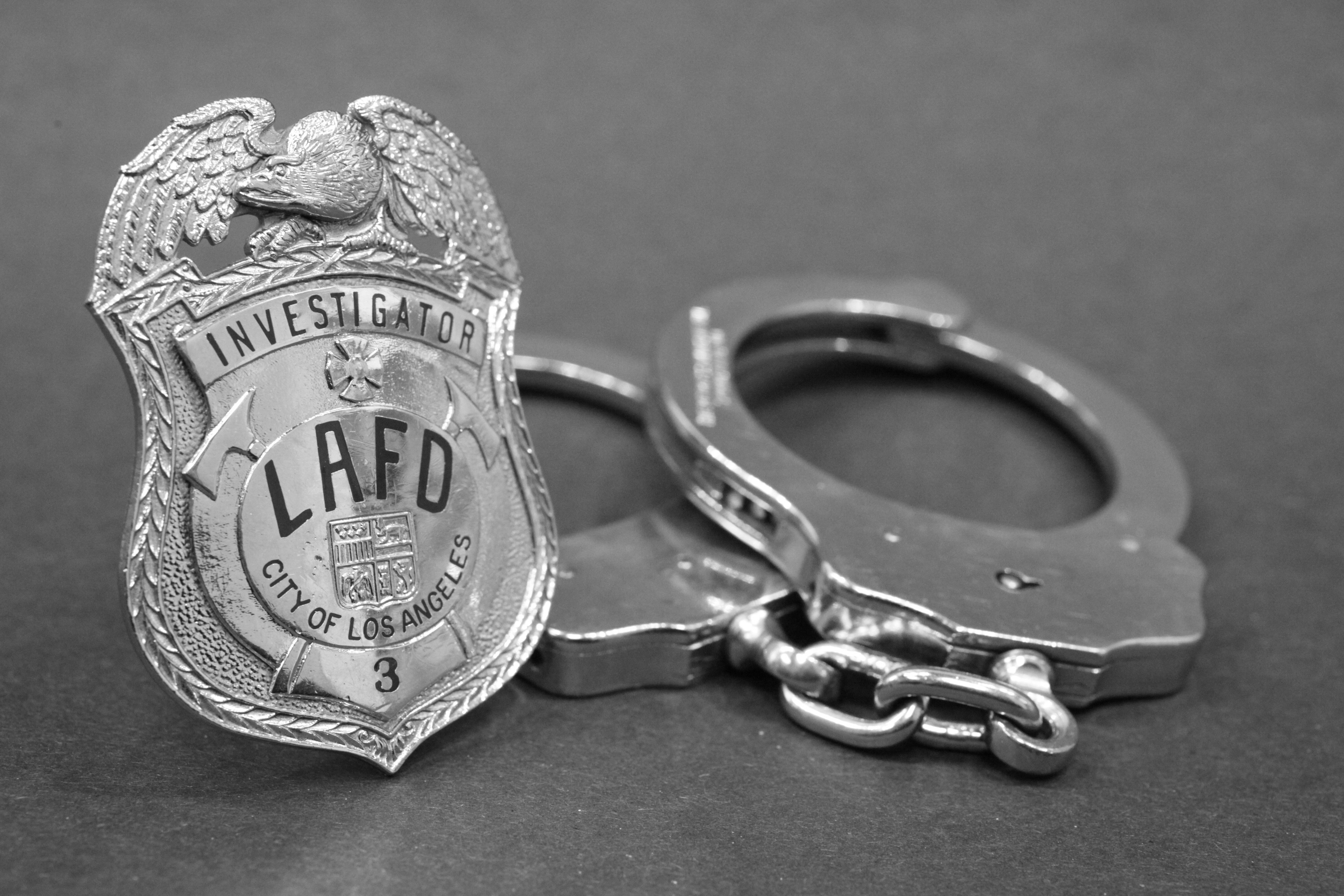 Stock photo of LAFD Investigator Badge in front of handcuffs.