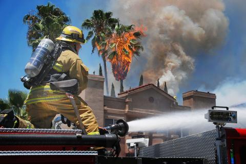 Firefighter on top of engine operating the wagon battery.  Large palm tree ablaze in front of structure