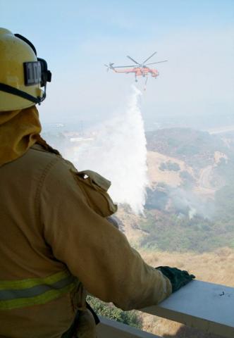 Firefighter watches helitanker in distance make water drops.
