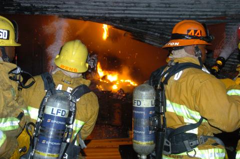 three firefighters in front of a rolling steel door cut open to show fire