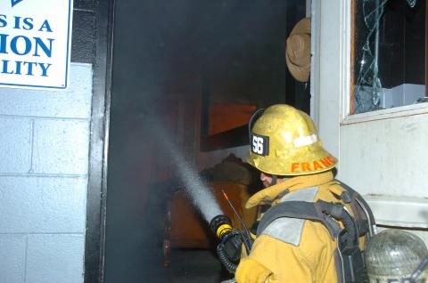 One firefighter with hose spraying water through door