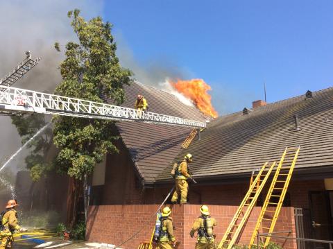 Aerial ladder extends to roof with firefighter on ladder and fire showing through the roof of large church