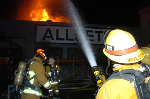 Firefighter with fire hose directing water to roof of building with fire showing