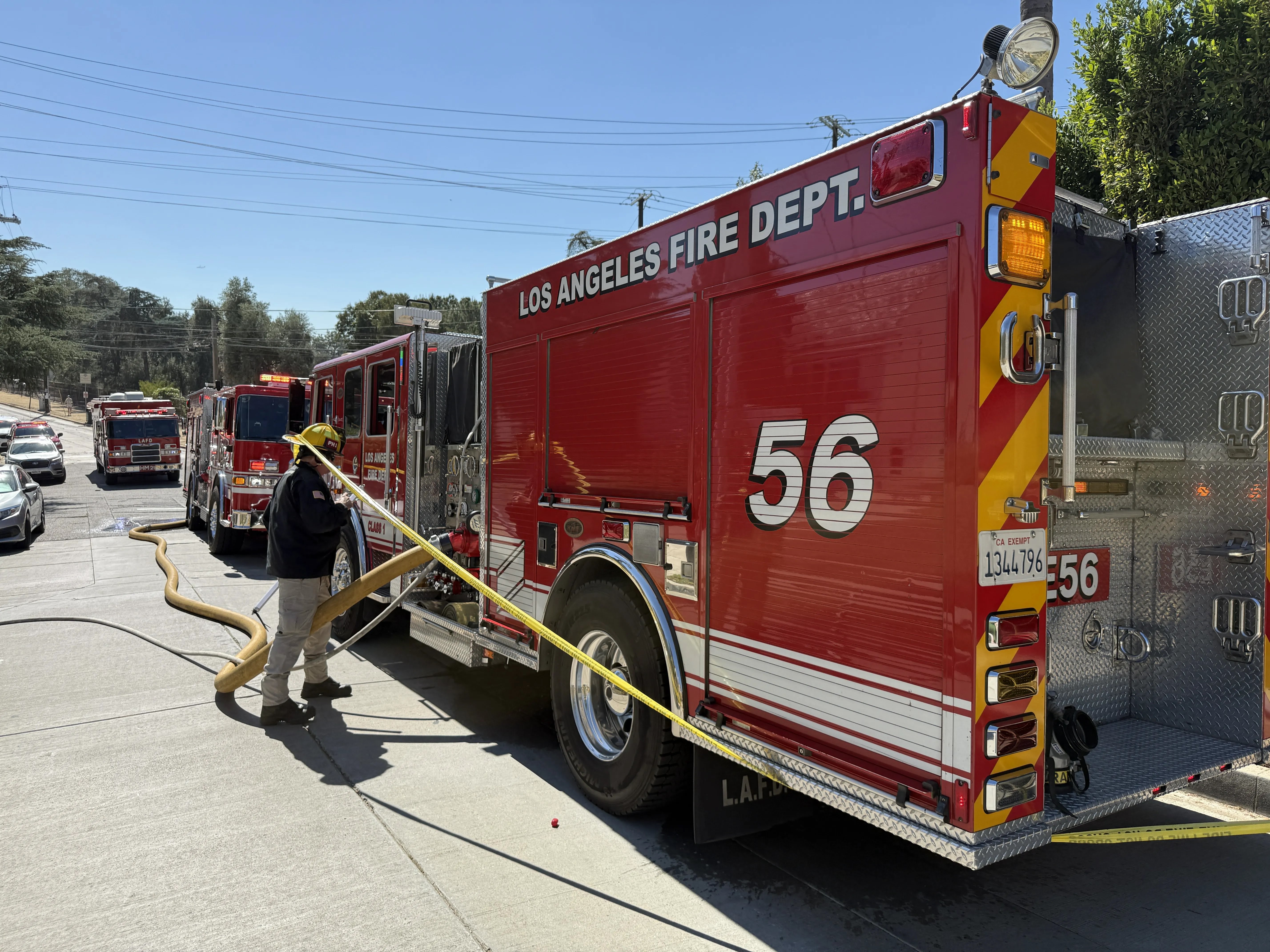 Firefighter operates supply lines connected to LAFD Engine 56 staged on street.