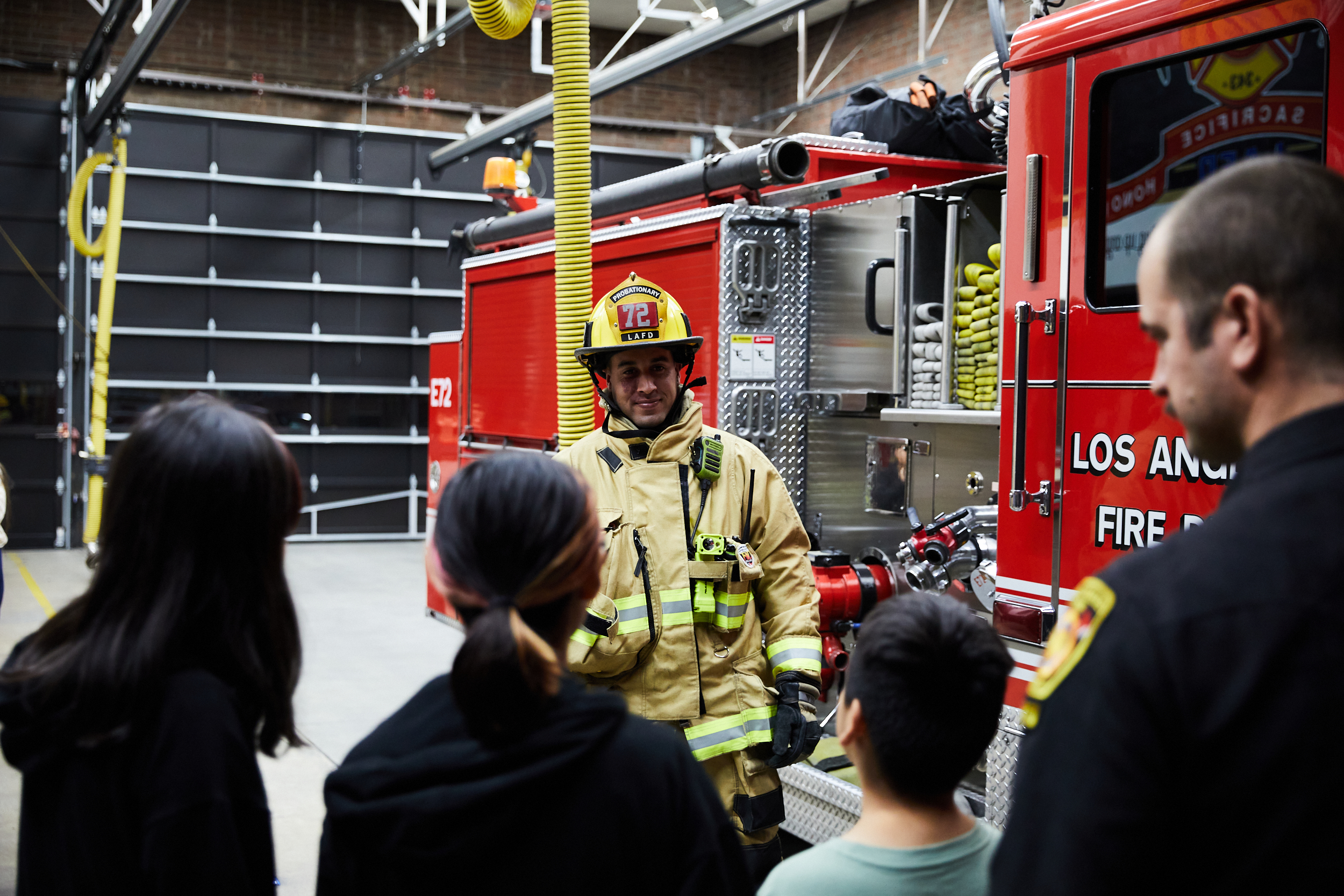 Firefighter pictured in full turnout gear with the families in the foreground and engine in the background