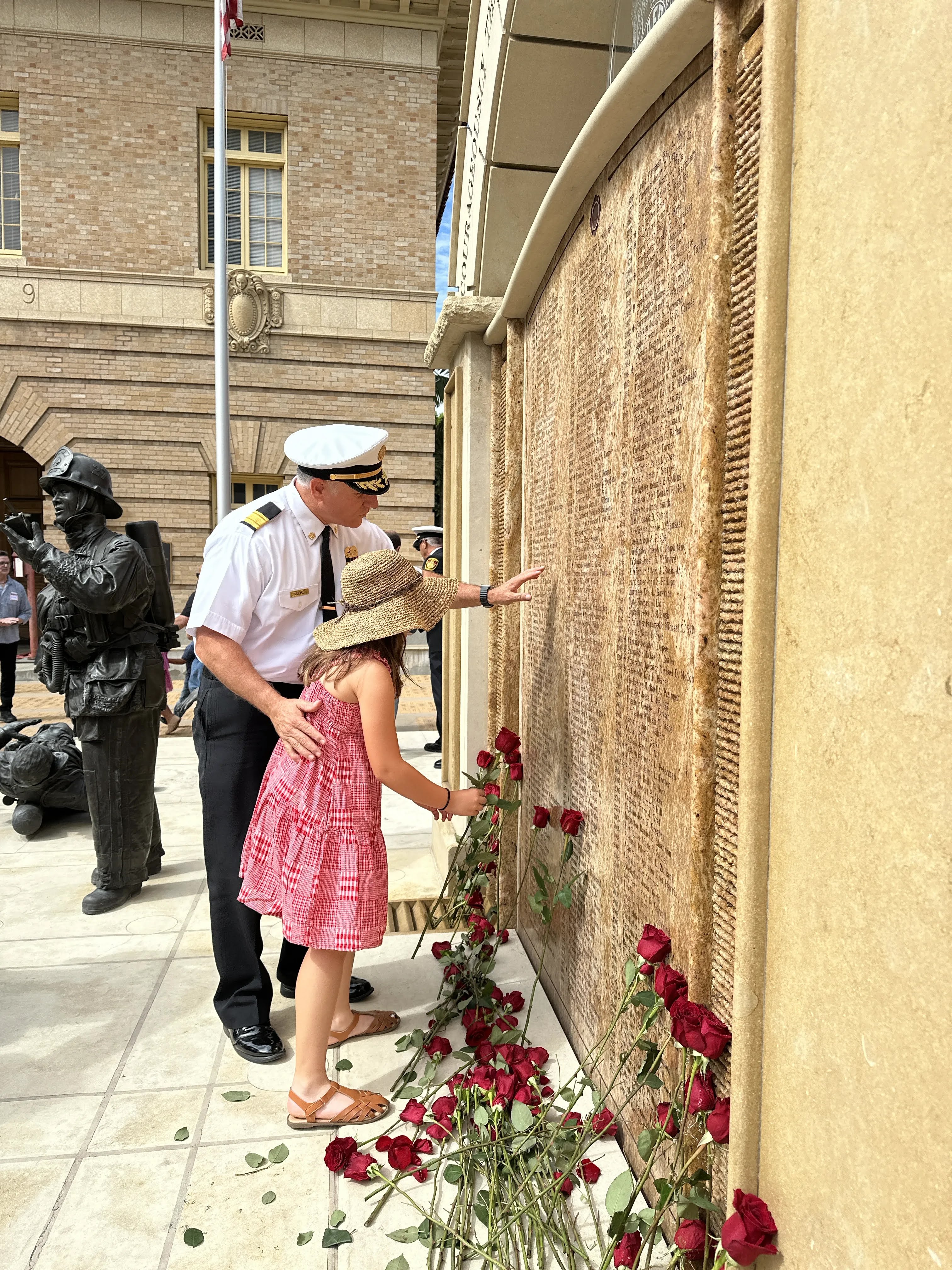 An officer and a child touching names inscribed on a stone fallen firefighters memorial wall at the LAFD Museum.